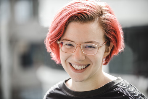 woman with pink hair and glasses smiling at the camera